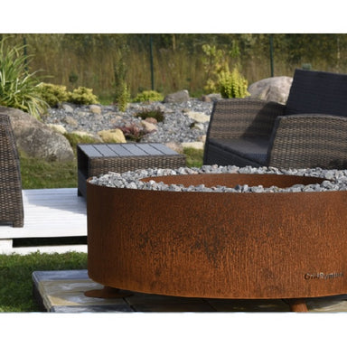 GrillSymbol Corten Steel Fire Pit Luna, ø 119 cm next to patio