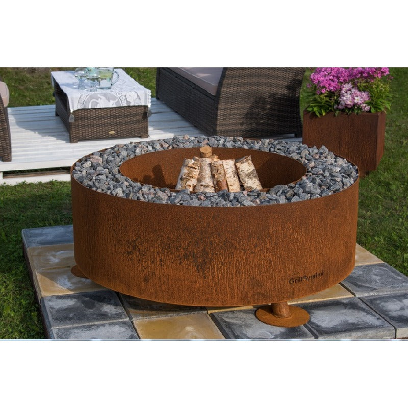 GrillSymbol Corten Steel Fire Pit Luna, ø 119 cm on patio with logs